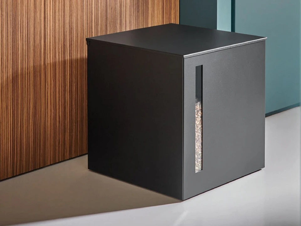 Un homme en pull bleu marine alimente un poêle à bois dans une cuisine moderne avec éléments en bois naturel