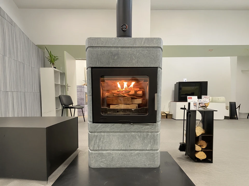 Intérieur chaleureux avec personne en pyjama à carreaux assise près d'un poêle à bois, tenant une tasse, chat noir au sol