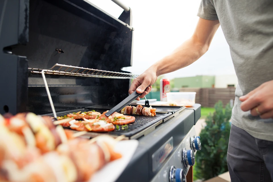 Scène de barbecue en plein air avec des brochettes colorées cuisant sur un grill à gaz