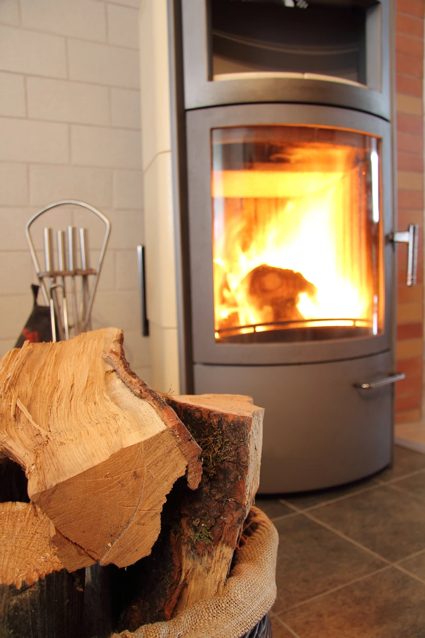 Un homme en pull bleu marine alimente un poêle à bois dans une cuisine moderne avec éléments en bois naturel